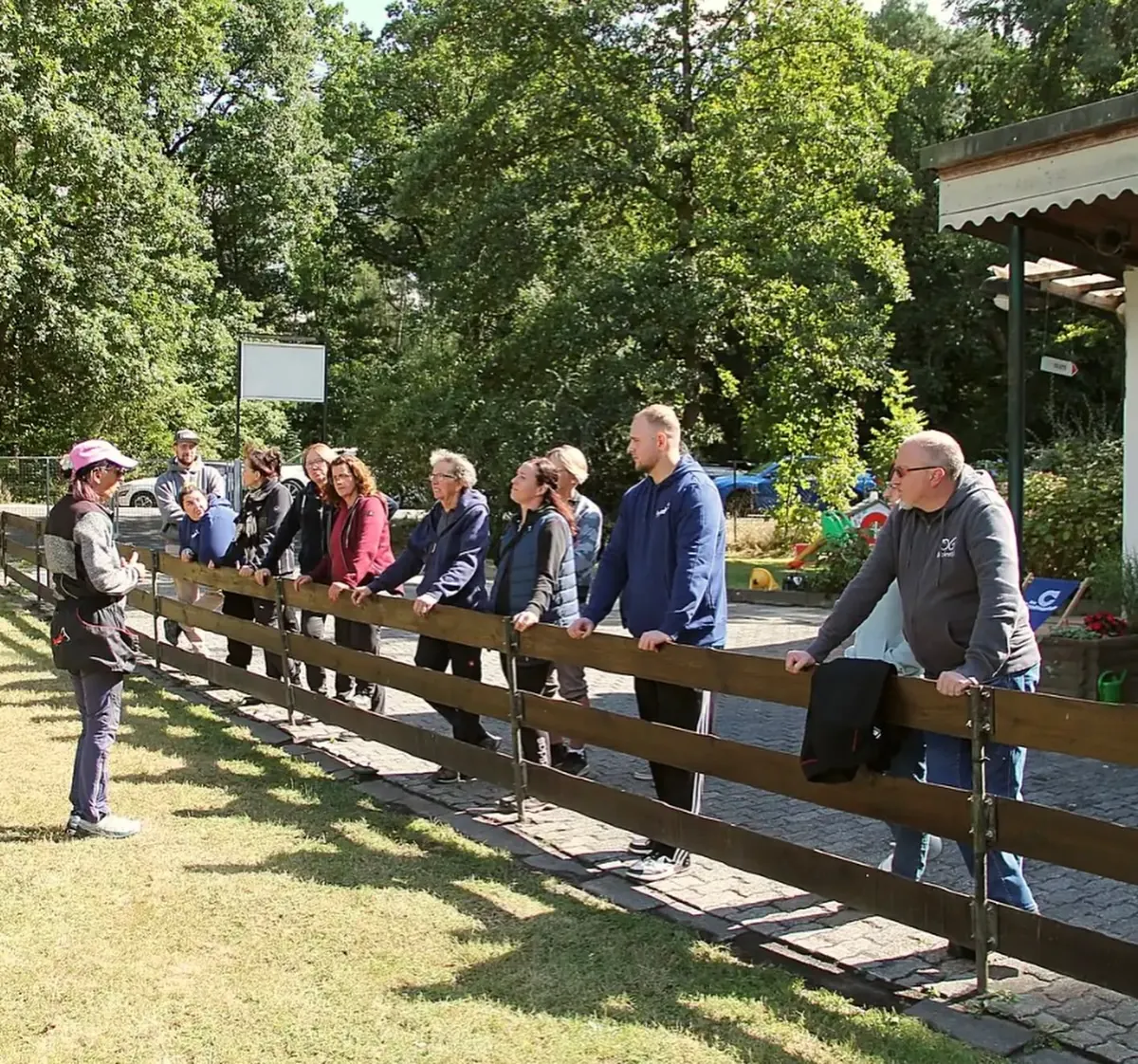 Teilnehmende schauen am Holzzaun zu